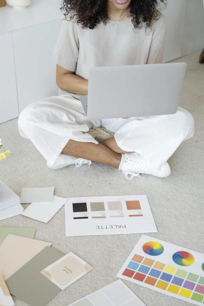 Young woman reviews color palettes for design project on laptop, sitting indoors.
